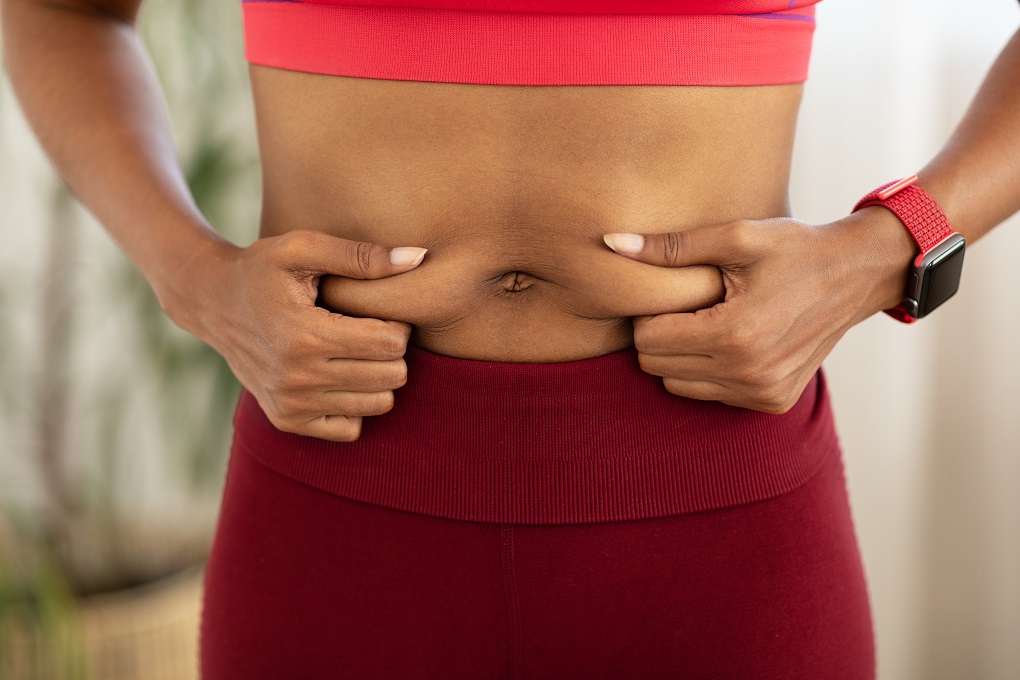 Belly Fat. Unrecognizable Black Woman Touching Stomach Losing Weight, Wearing Fitwear Standing Indoors. Cropped